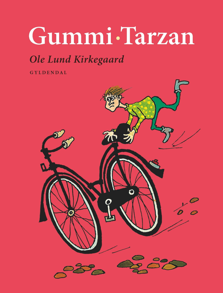 Bogen 'Gummi-Tarzan' af Ole Lund Kirkegaard viser en illustration af en dreng, der forsøger at cykle, mens han falder af cyklen. Baggrunden er fyldt med sten og en rød farve, der pryder bogens omslag.